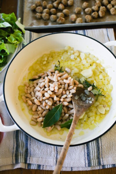 Sautéed onions, garlic, fresh bay leaves and rosemary in a white soup pot with beans.