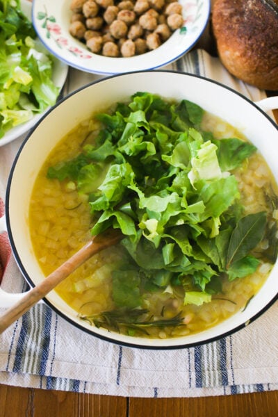 Sautéed onions, garlic, fresh bay leaves and rosemary in a white soup pot with beans and escarole.