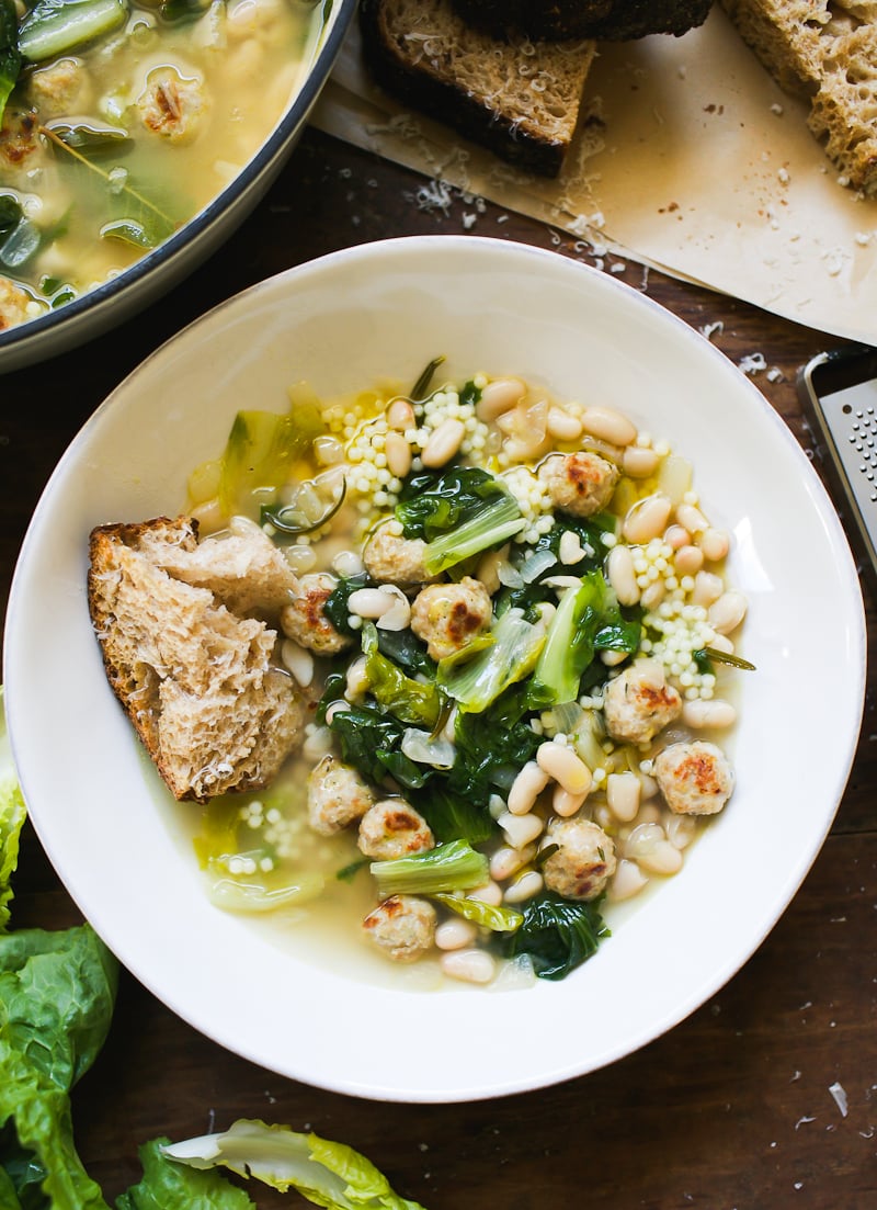Italian wedding soup with escarole, tiny chicken meatballs, and white beans in a bowl with crusty sourdough bread