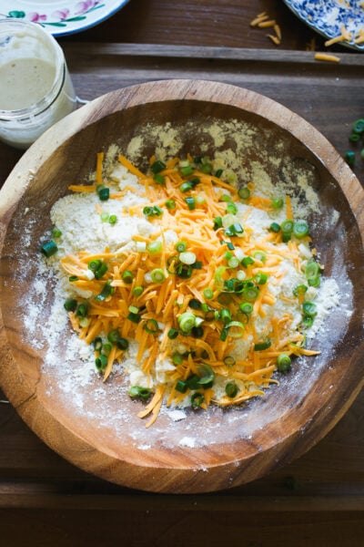 Finished sourdough biscuit dough with shredded cheddar cheese and sliced scallions on top