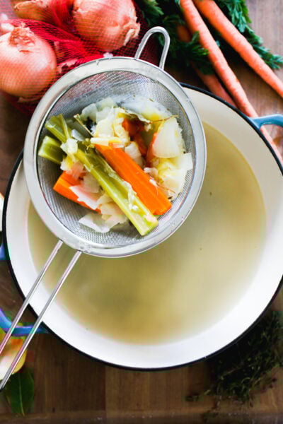 Italian vegetable stock ingredients in a strainer over a big soup pot