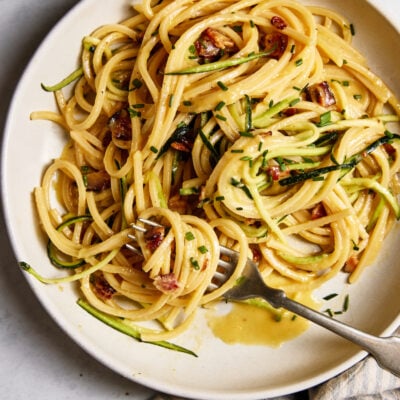 Homemade pasta carbonara with zucchini noodles, crispy bacon and a creamy egg sauce on a white plate.