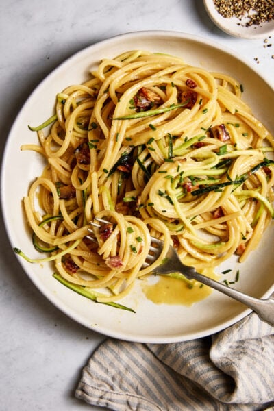 Homemade pasta carbonara with zucchini noodles, crispy bacon and a creamy egg sauce on a white plate.