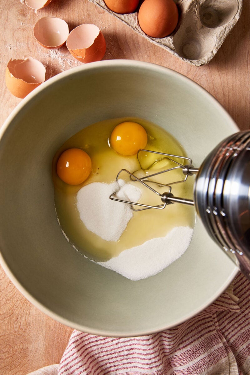Eggs and sugar in a large mixing bowl with a hand-held mixer.