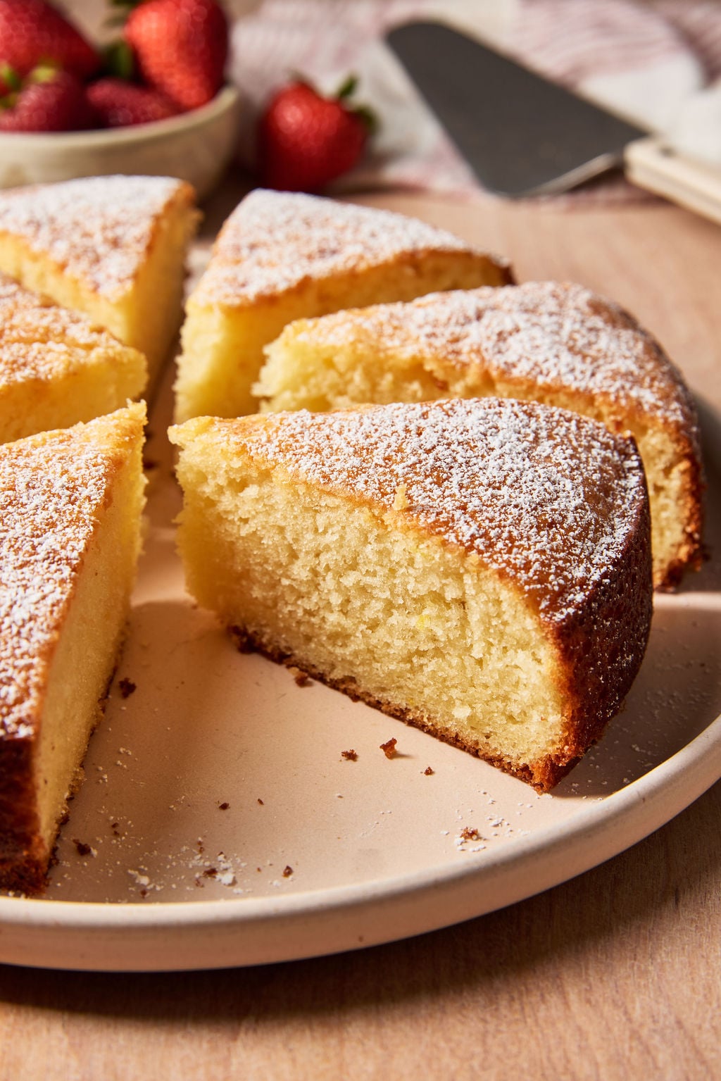 Sourdough French yogurt cake cut into thick slices, arranged on a pale pink plate with strawberries.
