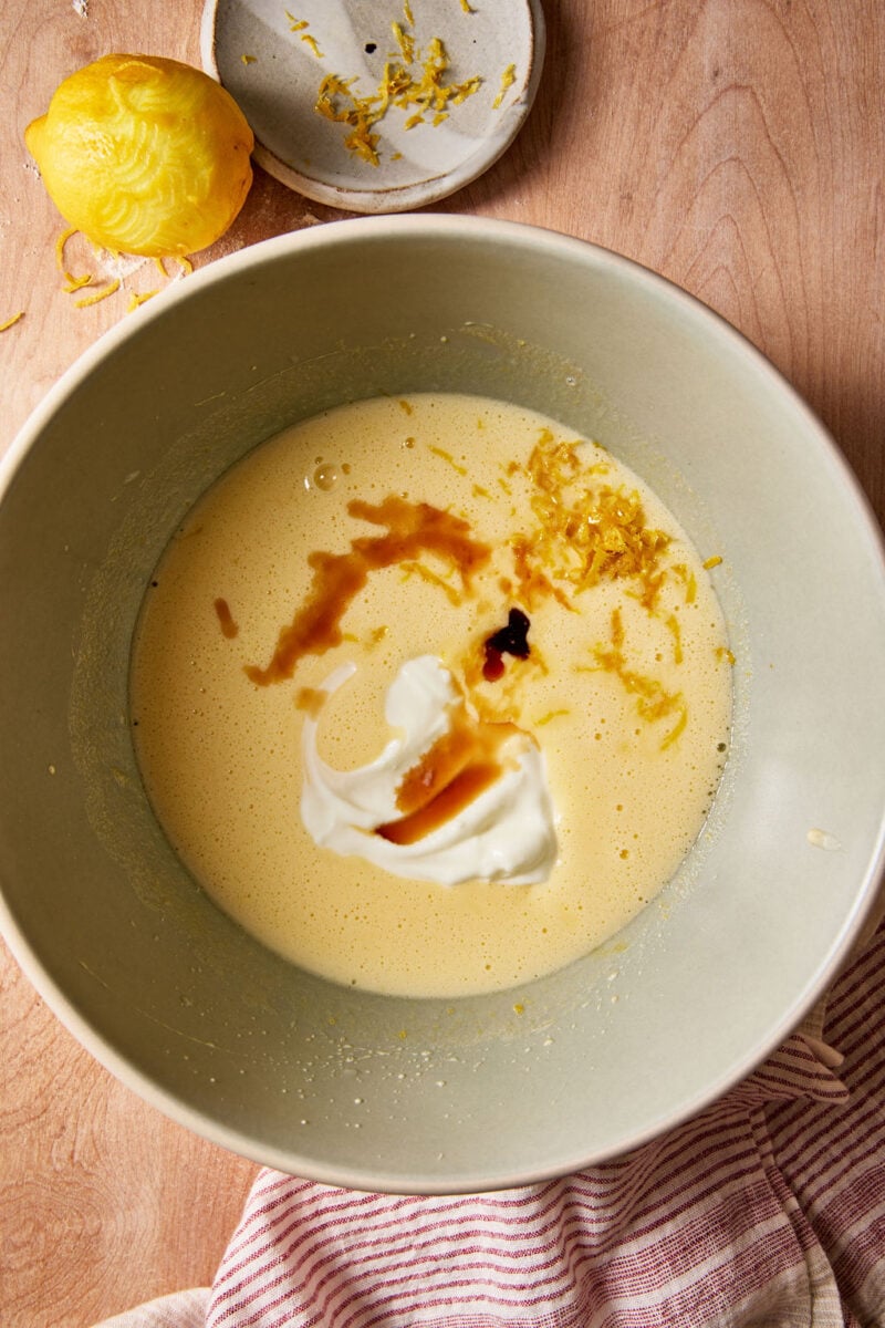 Sourdough French yogurt cake batter with whole milk yogurt, extracts, and lemon zest in a pale green mixing bowl.