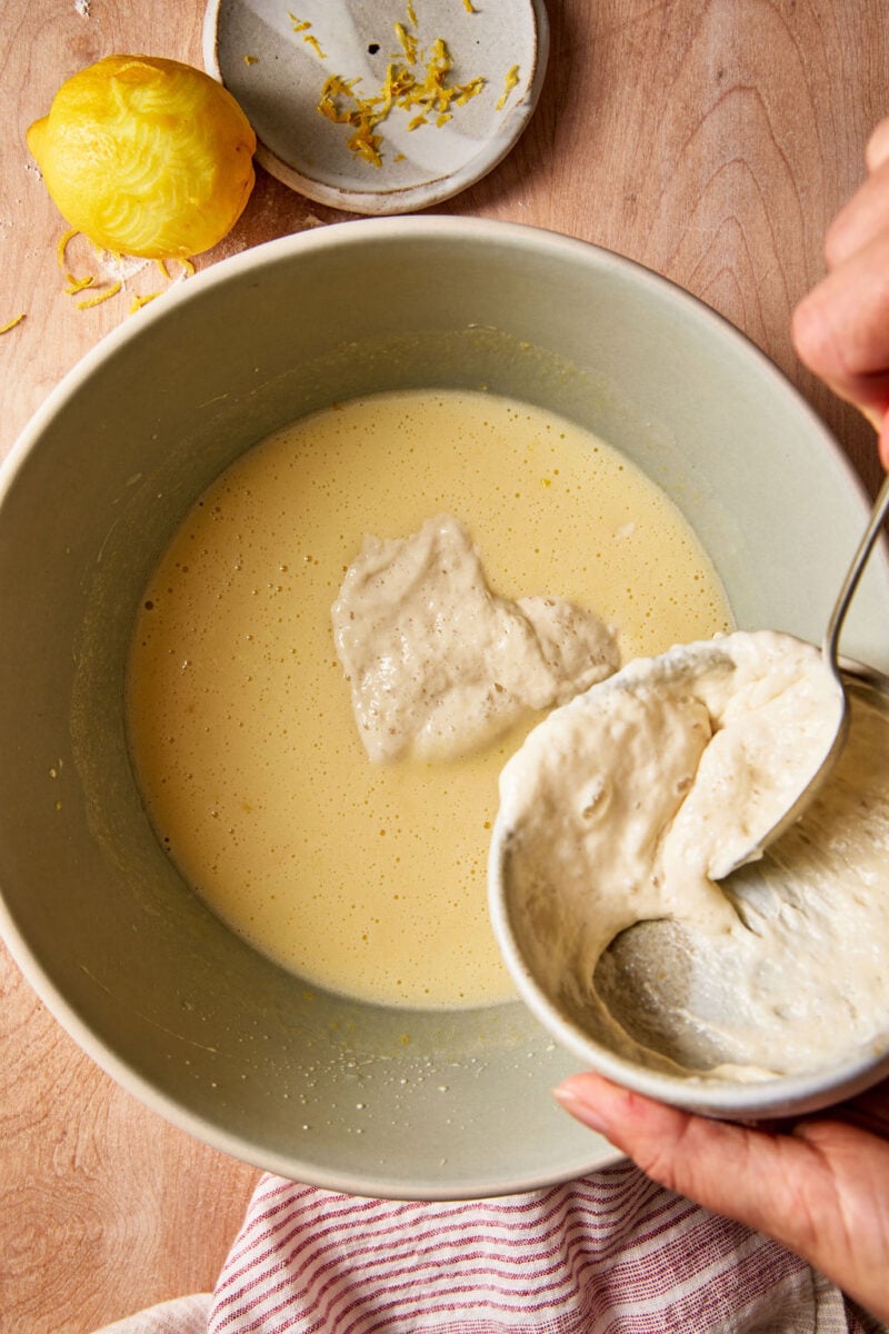 Adding sourdough discard to sourdough French yogurt cake batter in a pale green mixing bowl.