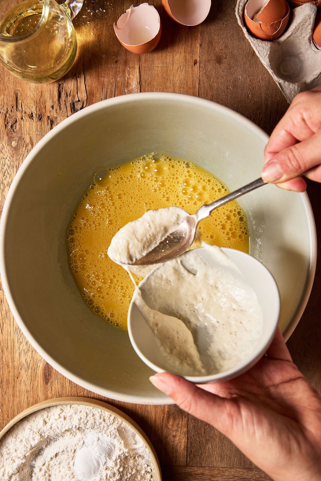 A spoonful of sourdough starter added to a large mixing bowl with whisked eggs