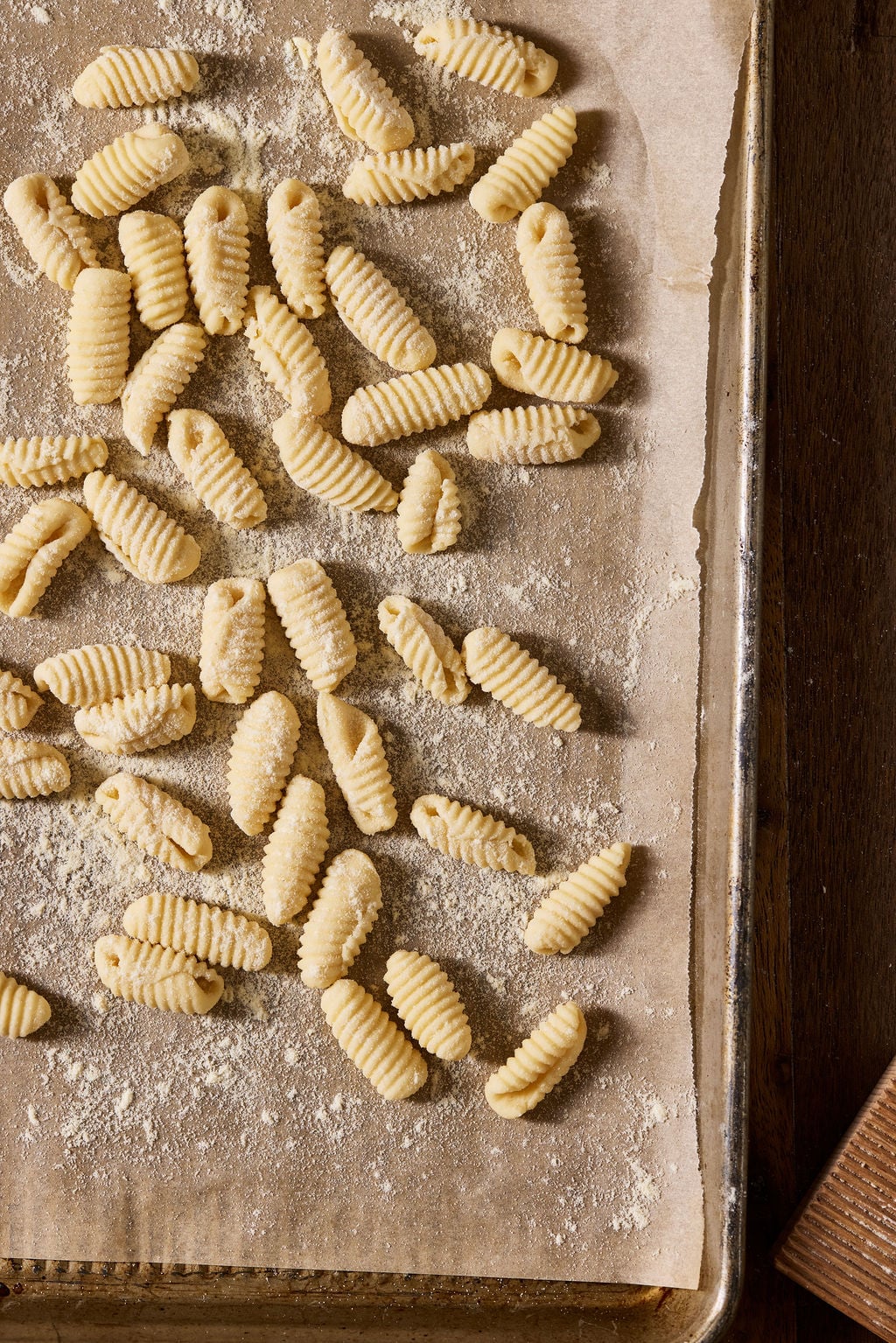Sourdough cavatelli, dusted in semolina flour, arranged on a brown parchment-lined sheet pan.