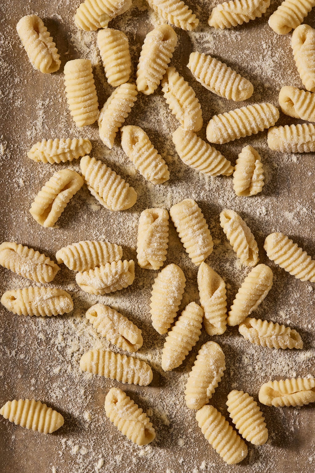 Sourdough cavatelli, dusted in semolina flour, arranged on a brown parchment-lined sheet pan.
