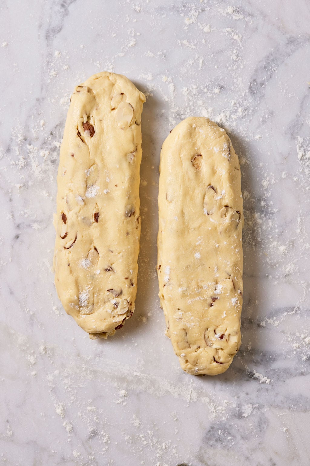 Sourdough biscotti dough shaped into two logs on a marble surface.