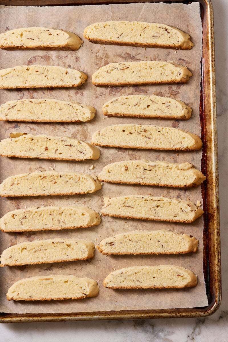 Tray of sliced sourdough biscotti on a parchment lined sheet pan in preparation for the final bake.