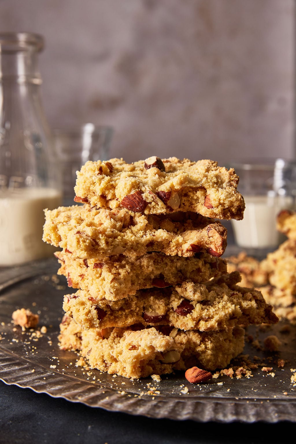 Sbrisolona (crunchy Italian almond crumble cookie) broken into rustic pieces and stacked on top of each other with cold glasses of milk in the background.