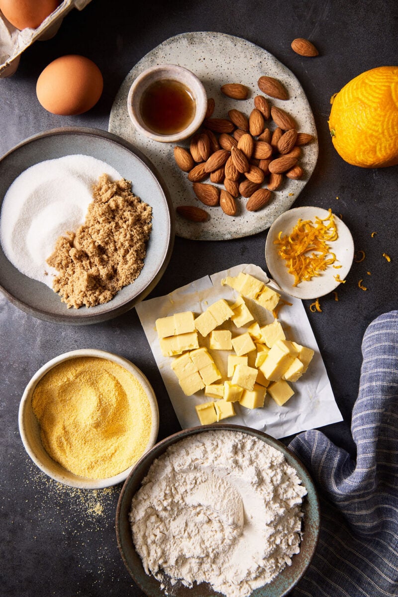 Sbrisolona ingredients: cornmeal, flour, sugar, butter, almonds, orange zest, and almond and vanilla extracts.