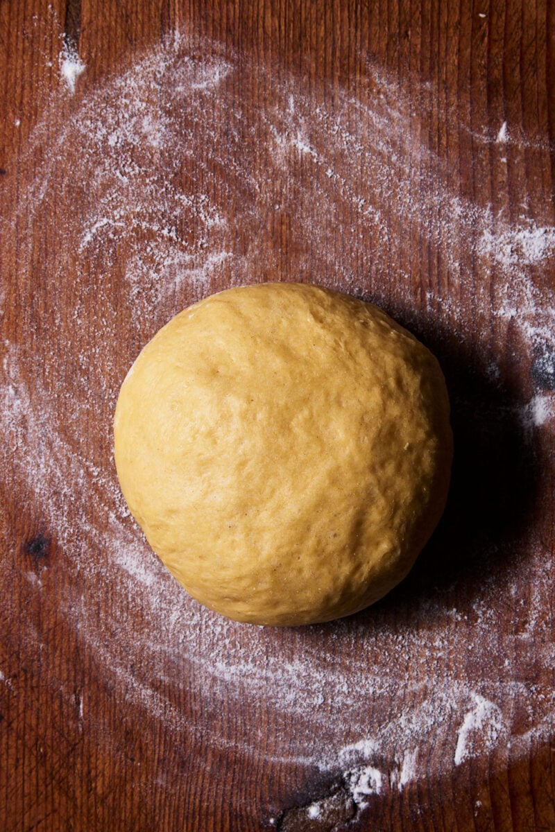 Ball of sourdough mafaldine pasta dough on a flour-dusted wooden surface