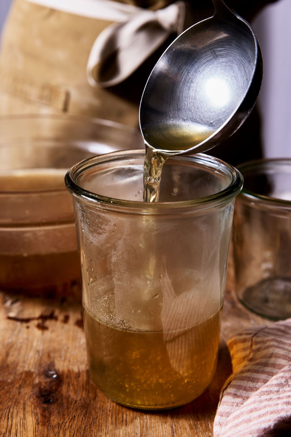 Ladling Italian chicken brodo into a tall glass jar.