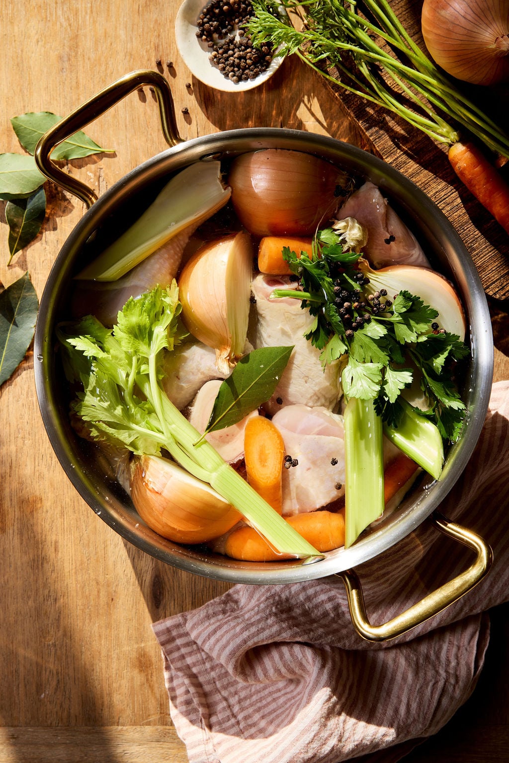 Italian chicken brodo ingredients, in a heavy bottom stock pot: chicken legs and thighs, onions, carrots, bay leaves and celery and peppercorns.