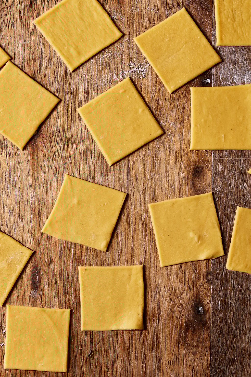 Cut pasta squares, 2x2-inch, on a wooden surface.