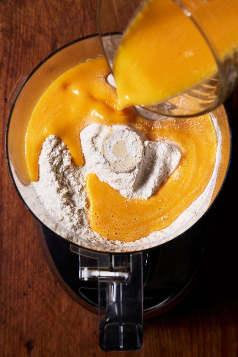 Flour, eggs, and sourdough starter in the bowl of a food processor.
