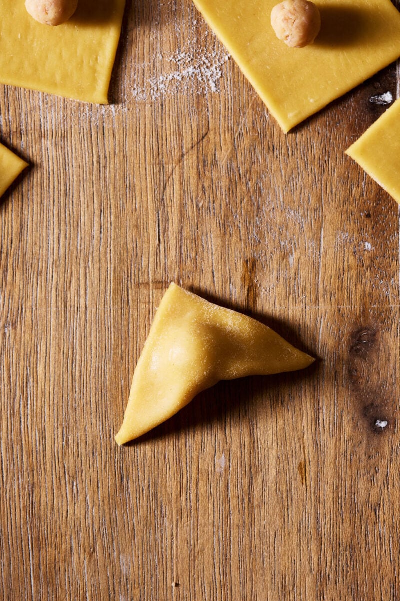 Sourdough tortellini folded into a triangle on a wooden surface.