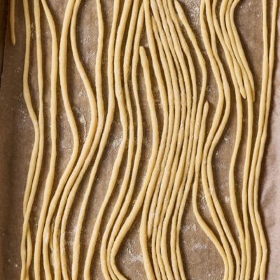 Sourdough pici pasta on a semolina dusted, parchment-lined sheet pan.