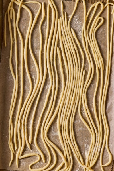 Sourdough pici pasta on a semolina dusted, parchment-lined sheet pan.