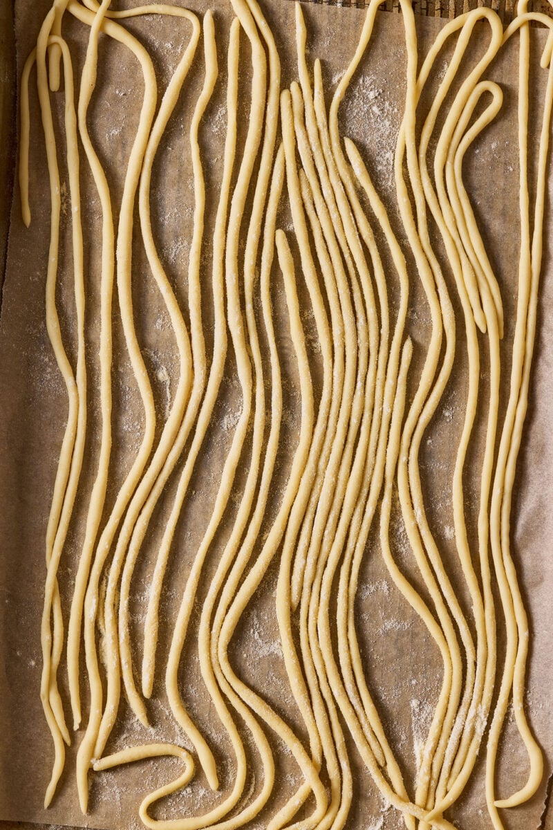 Sourdough pici pasta on a semolina dusted, parchment-lined sheet pan.