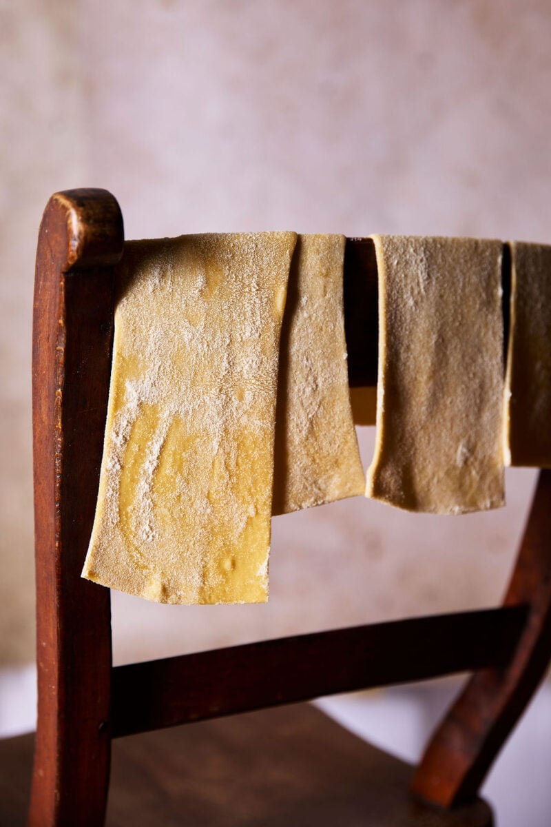 Sourdough mafaldine pasta sheets hanging over the back of a wooden chair to semi-dry