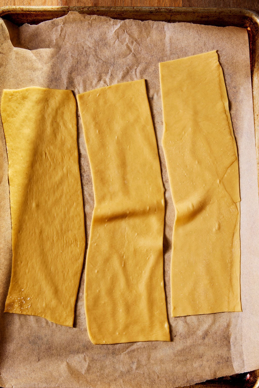 Rolled pasta sheets for sourdough tortellini in a parchment-lined sheet pan.