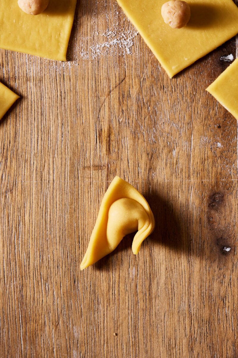 Wrapping a corner of the folded sourdough tortellini to meet the other corner.