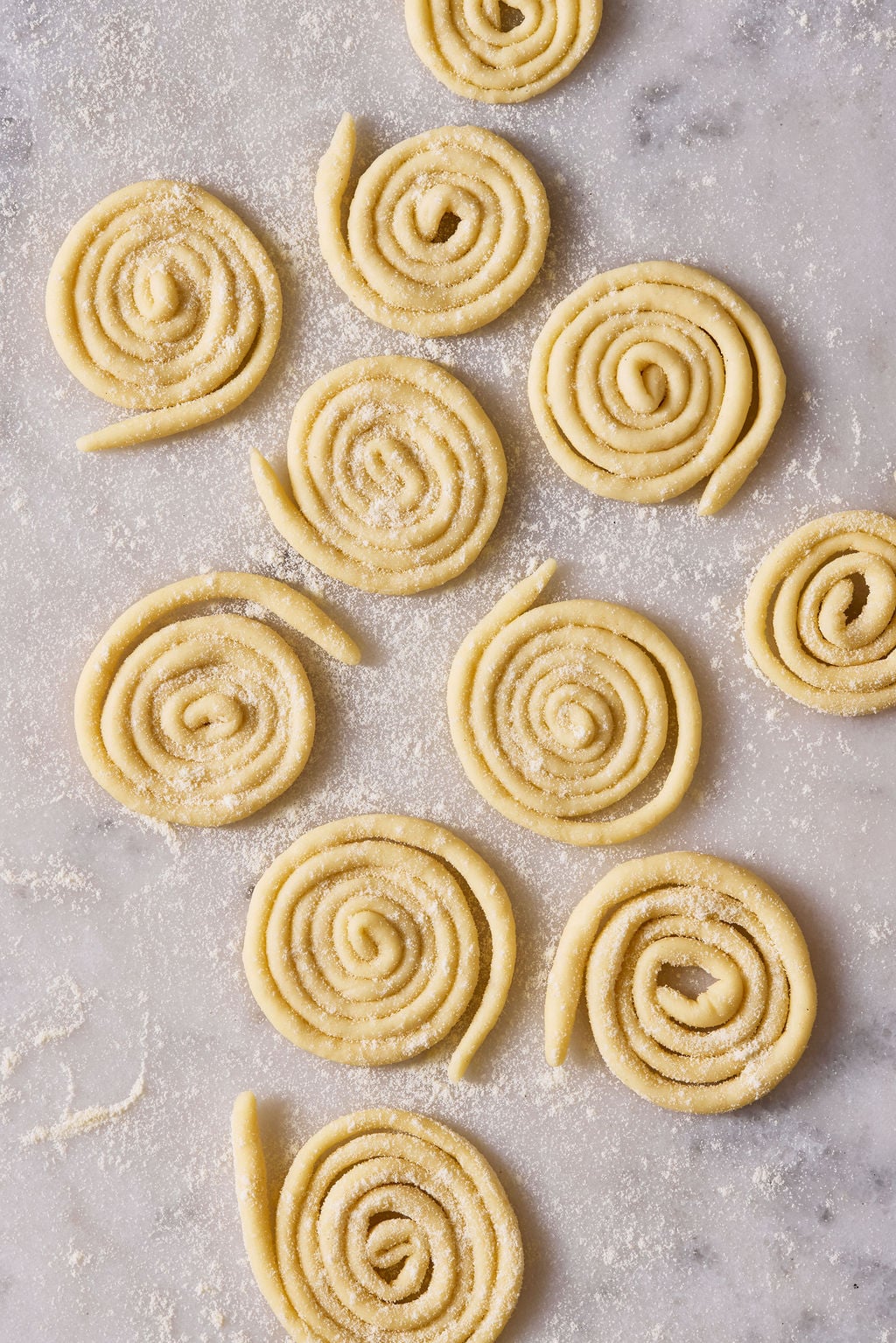 Sourdough pici pasta, arranged in coils, on a semolina-dusted marble surface.