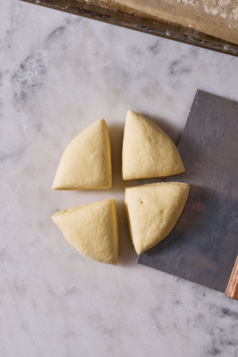 Sourdough pici pasta dough cut into 4 pieces on a marble surface.