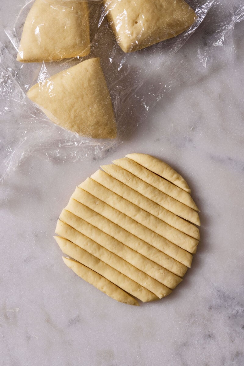 Sourdough pici pasta dough flattened, and cut across into 1/4-inch wide strips on a marble surface.