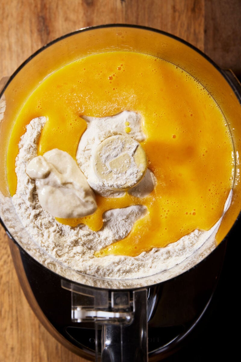Sourdough tortellini ingredients: Italian 00 flour, beaten eggs, and sourdough starter in a food processor on a wooden surface.