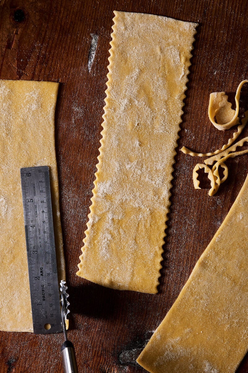 Trimming sourdough mafaldine pasta sheets by hand with a fluted pastry wheel and a ruler.