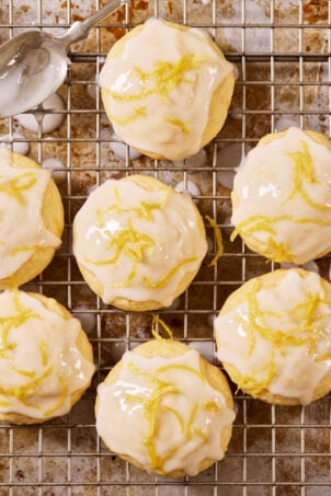 Glazed sourdough lemon drop cookies with lemon zest on a wire rack set over a sheet pan, with a metal spoon.