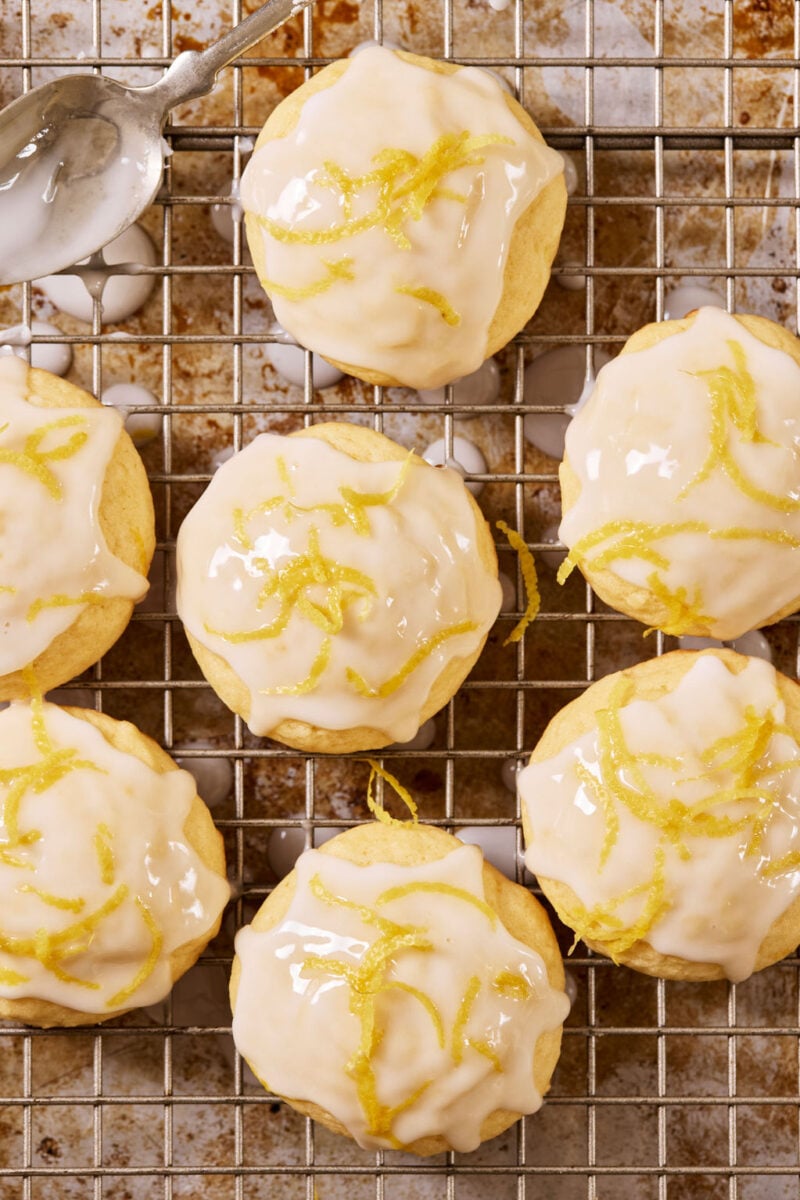 Glazed sourdough lemon drop cookies with lemon zest on a wire rack set over a sheet pan, with a metal spoon.