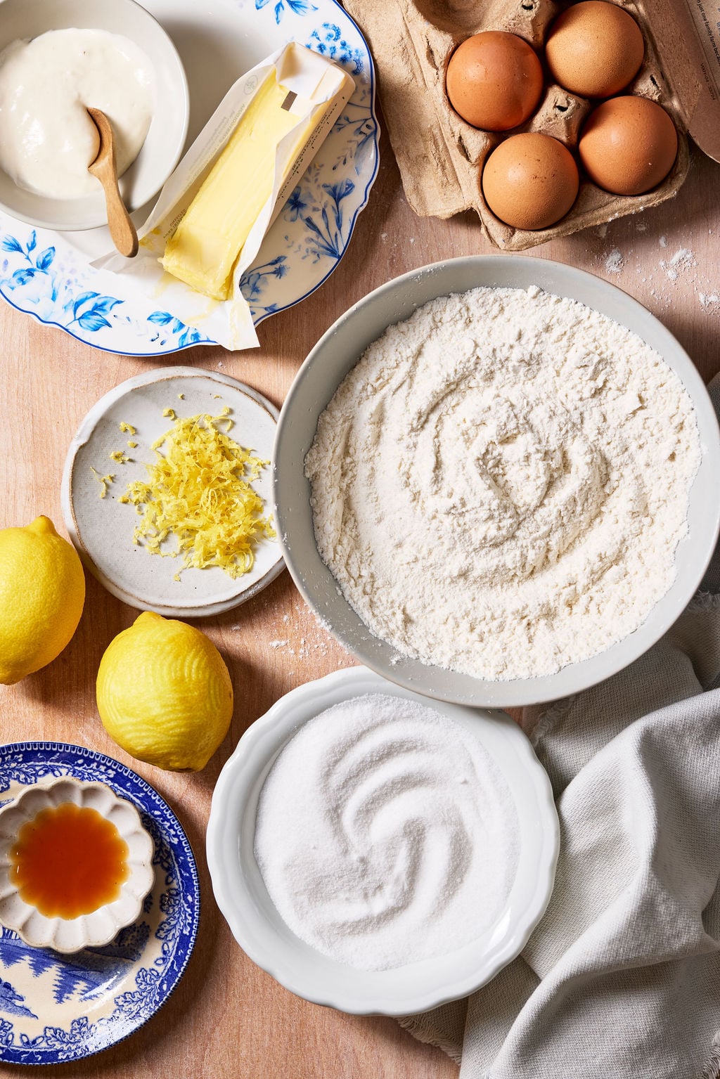 Sourdough lemon drop cookie ingredients: flour, sugar, butter, brown eggs, lemons, lemon zest, vanilla and sourdough discard on a rustic wooden surface.