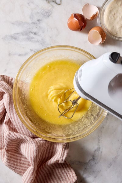 Beaten eggs and sugar in a glass mixing bowl with a hand-held electric mixer.