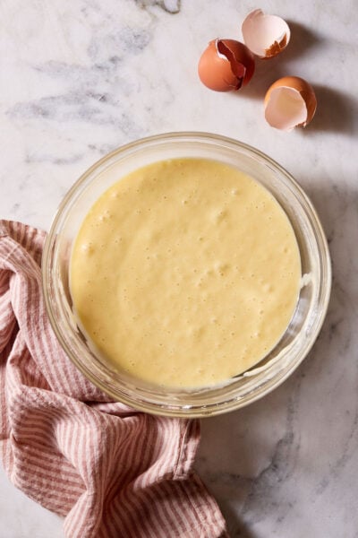 Finished, mixed sourdough cupcake batter in a large glass bowl on a marble surface with a red-striped linen kitchen towel.