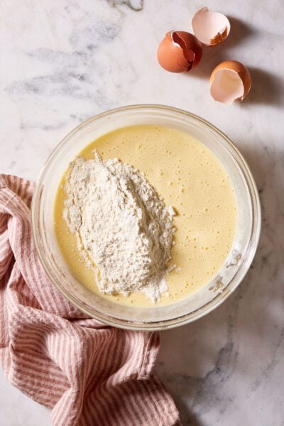 Sourdough cupcake batter with flour in a large glass bowl, set on a marble surface with a red-striped linen kitchen towel.