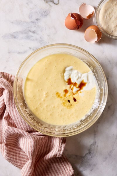 Sourdough French yogurt cupcake batter with yogurt and vanilla extract, set on a marble surface with a red-striped linen kitchen towel and egg shells.