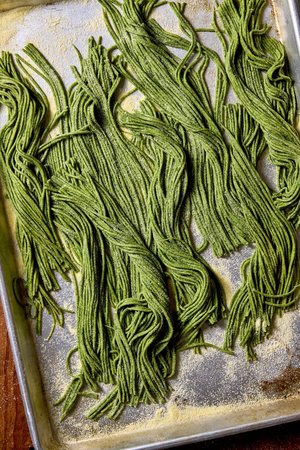 Homemade sourdough spinach pasta on a metal sheet pan dusted with semolina flour