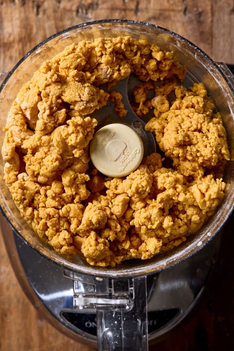 A food processor bowl filled with a crumbly, orange sourdough pumpkin pasta dough.