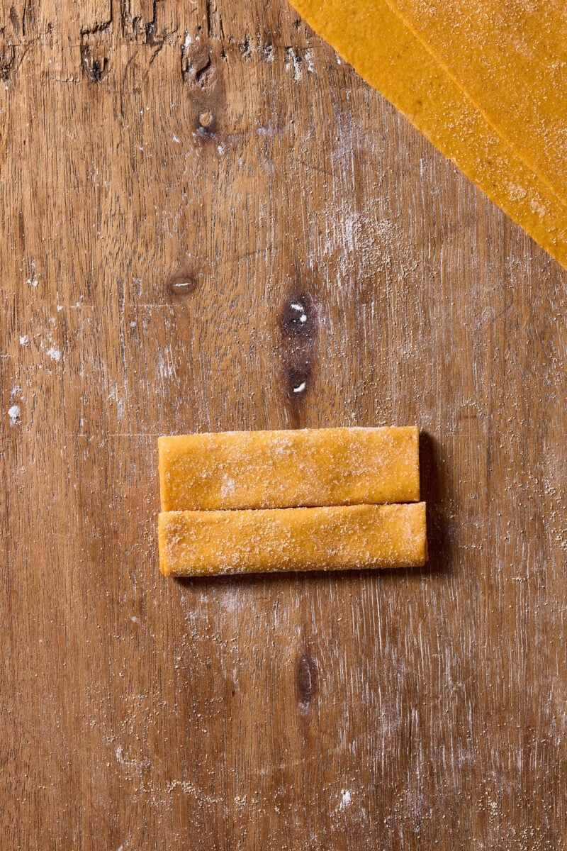 Folded fresh sourdough pumpkin pasta dough resting on a floured wooden surface.
