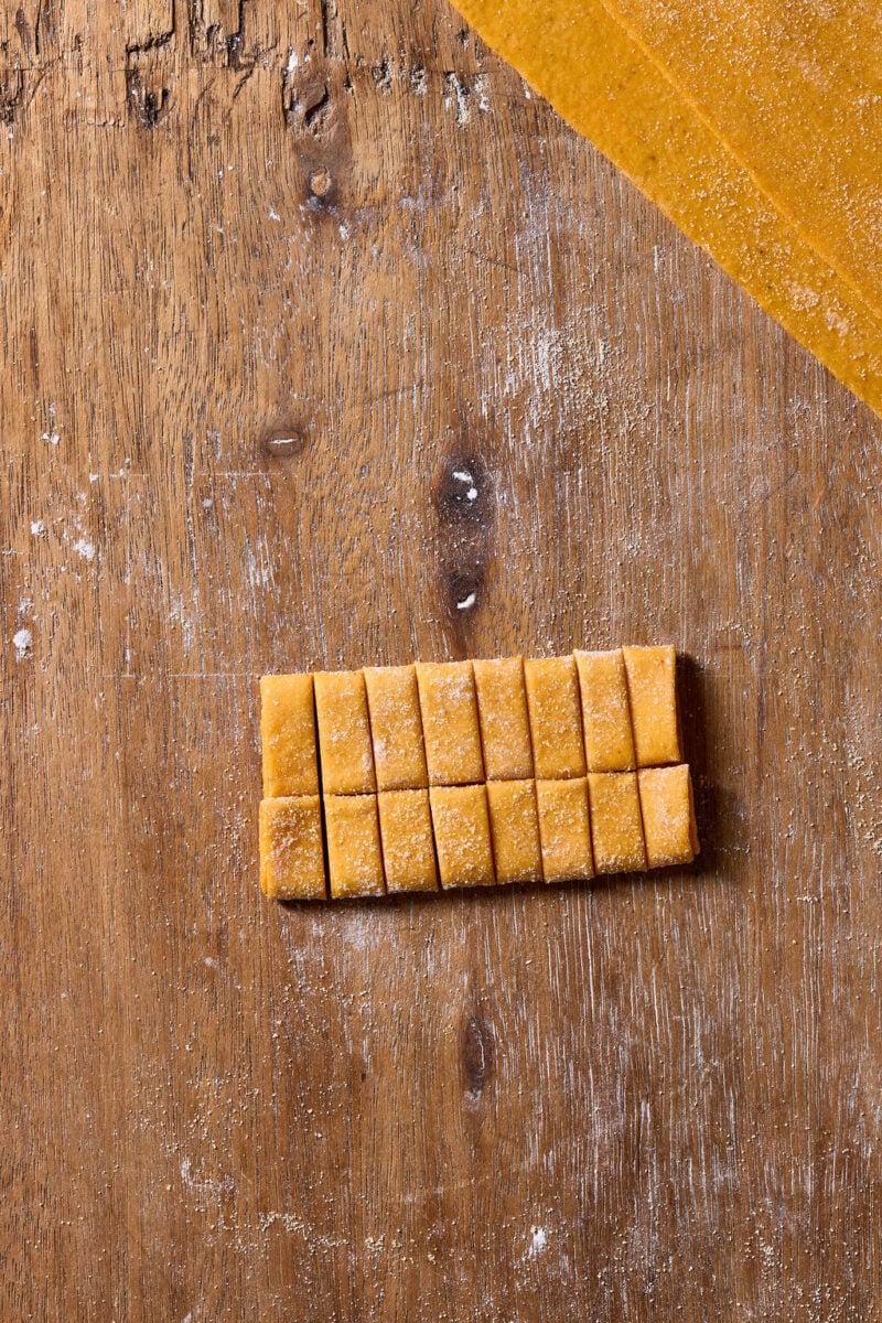 Fresh sourdough pumpkin pasta dough cut into small, uniform rectangular pieces arranged on a floured wooden surface.