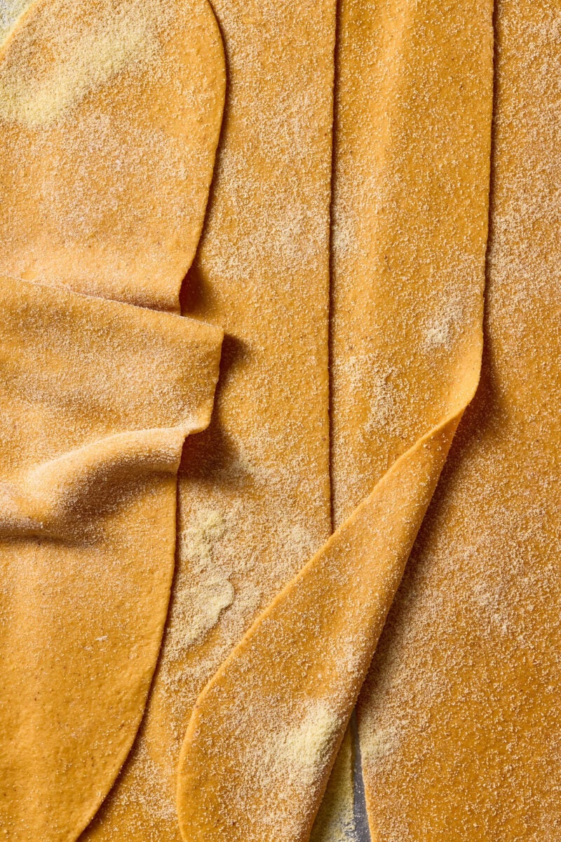 Sheets of rolled-out fresh sourdough pumpkin pasta dusted with flour.